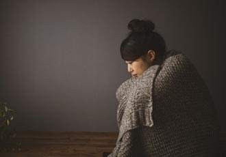薄暗い部屋で膝を抱えて座る女性の横顔